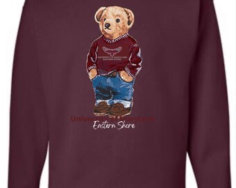 May include: Burgundy sweatshirt with a teddy bear illustration. The bear wears a maroon sweater and blue jeans. The sweater has the text "University of Maryland Eastern Shore". The bear is wearing brown shoes.