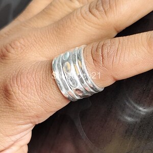 K&ouml;nnte beinhalten: Ein silberner Ring mit geh&auml;mmerter Textur, bestehend aus vier &uuml;bereinanderliegenden B&auml;ndern. Der Ring hat ein einzigartiges, organisches Aussehen.