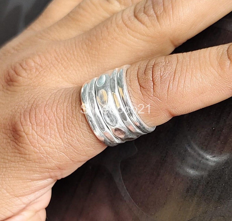 K&ouml;nnte beinhalten: Ein silberner Ring mit geh&auml;mmerter Textur, bestehend aus vier &uuml;bereinanderliegenden B&auml;ndern. Der Ring hat ein einzigartiges, organisches Aussehen.