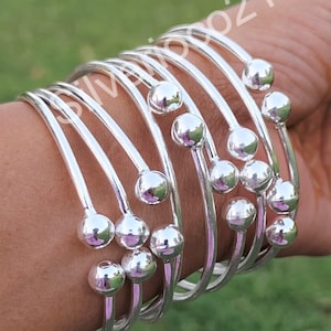 May include: A set of silver bangles with small round beads. The bangles are stacked on top of each other and are worn on a person's wrist.