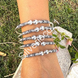 May include: Five silver bangles with a textured design and a small ball accent on each bangle.