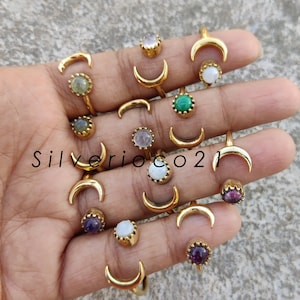 May include: A selection of gold-coloured nose rings and crescent moon-shaped jewellery. The rings feature various gemstones, including green, purple, and white stones. The text "Silverioco21" is visible.