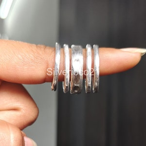 May include: Five silver rings stacked on a finger. The rings are all different widths and have a hammered texture.
