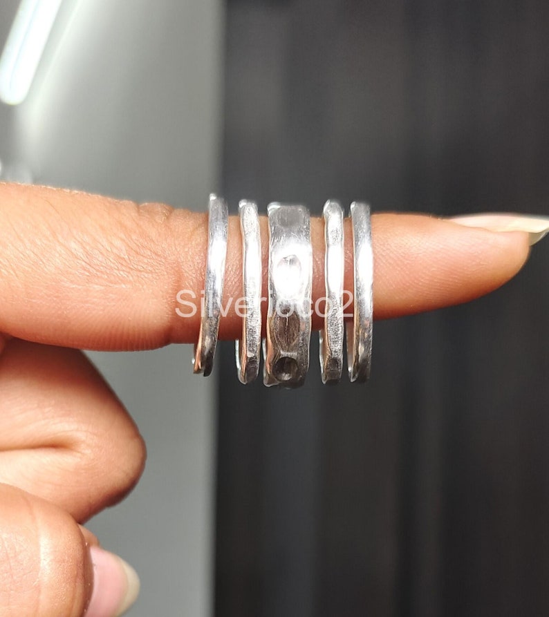 K&ouml;nnte beinhalten: F&uuml;nf silberne Ringe, die auf einem Finger &uuml;bereinander liegen. Die Ringe haben alle unterschiedliche Breiten und eine geh&auml;mmerte Textur.