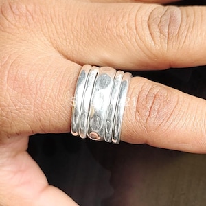 K&ouml;nnte beinhalten: Ein silberner Ring mit geh&auml;mmerter Textur. Der Ring besteht aus mehreren &uuml;bereinander gestapelten B&auml;ndern.