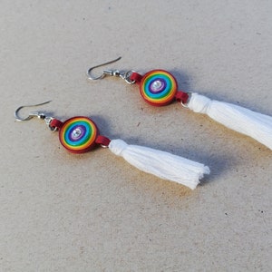 May include: A pair of rainbow-colored earrings with white tassels. The earrings are made of paper and have a silver hook.