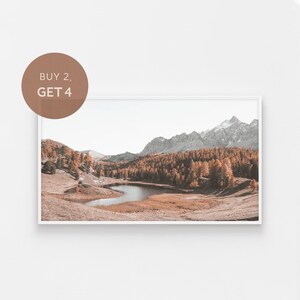 Pode incluir: Uma fotografia de paisagem que apresenta um rio sinuoso que flui através de um vale cercado por árvores verdes exuberantes e montanhas cobertas de neve no fundo.