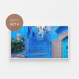 Op de afbeelding: Een smalle, blauw geverfde steeg in een Marokkaanse stad met een trap die naar een deur leidt. De muren zijn versierd met ingewikkelde tegelpatronen.