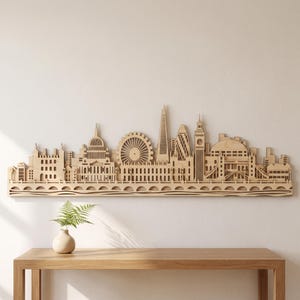 Pode incluir: Uma peça de arte de parede em madeira cortada a laser que retrata o horizonte de Londres, apresentando marcos reconhecíveis como o London Eye, The Shard, Big Ben e a Tower Bridge, montados numa base horizontal com um design de ponte.