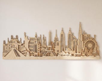 May include: A light-colored wooden wall art piece featuring a detailed laser-cut skyline composed of various global landmarks, including the Eiffel Tower, the Statue of Liberty, the Colosseum, the Sydney Opera House, and a large Ferris wheel.