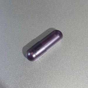 May include: A single dark purple capsule pill.