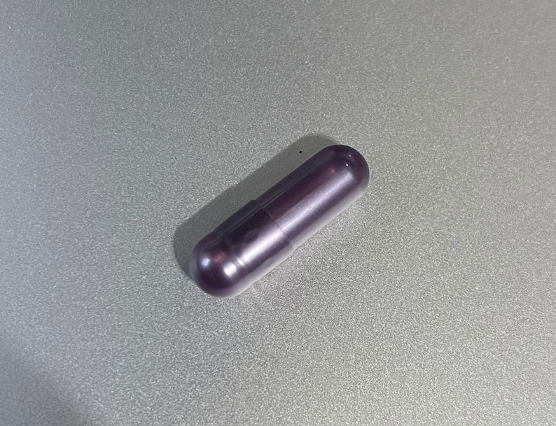 May include: A single dark purple capsule pill.