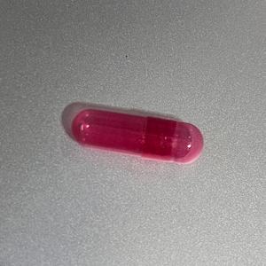May include: A single pink capsule containing a clear, slightly cloudy liquid.