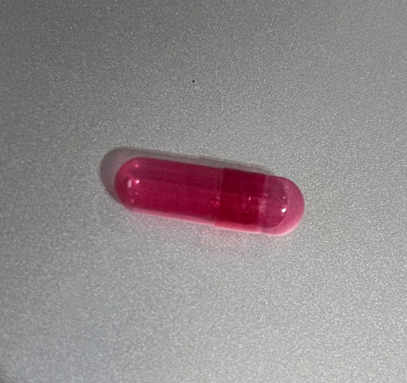 May include: A single pink capsule containing a clear, slightly cloudy liquid.