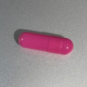 May include: A single pink capsule pill.