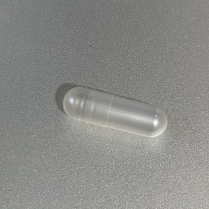 May include: A clear plastic capsule, commonly used for holding small items or samples.
