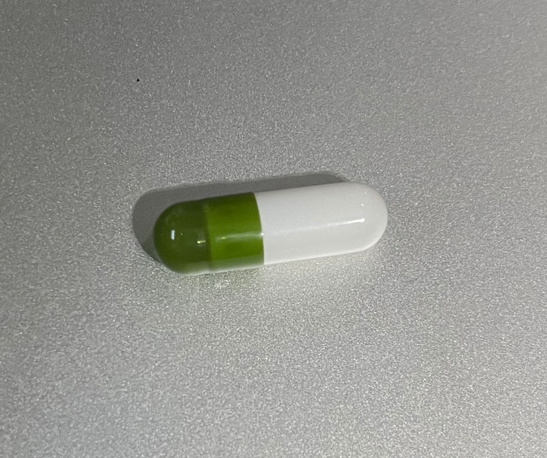 May include: A green and white capsule pill.