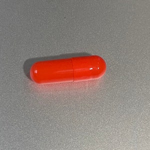 May include: A single bright orange capsule pill.