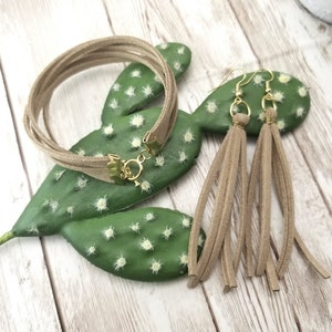 May include: A set of brown suede jewelry featuring a multi-strand bracelet and tassel earrings.