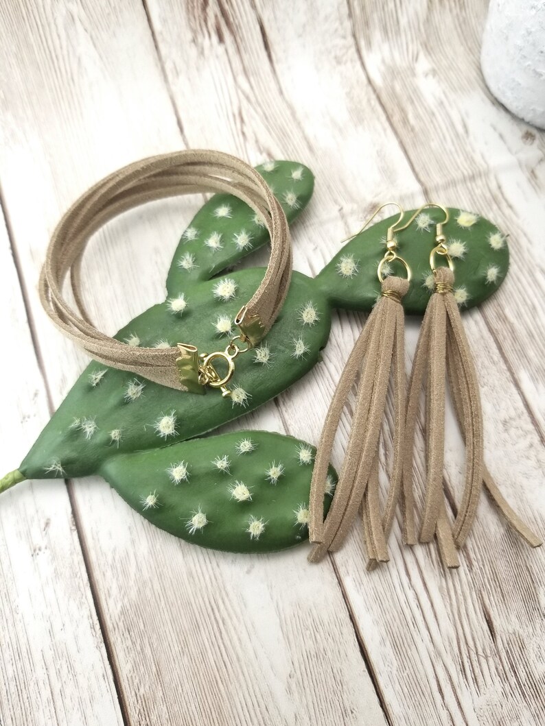 May include: A set of brown suede jewelry featuring a multi-strand bracelet and tassel earrings.
