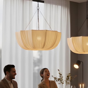 Op de afbeelding: Een eethoek met een donkere houten tafel, stoelen en twee hanglampen. Drie personen zitten aan tafel en genieten van een maaltijd. De kamer heeft een neutraal kleurenpalet met een groot raam en kunstwerken aan de muur.