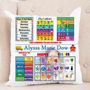 May include: A white pillow with colorful educational charts for days of the week, alphabet, numbers 1-10, months of the year, shapes, and colors. The pillow has a personalized message that says "THIS LEARNING PILLOW BELONGS TO: Alyssa Marie Dow".