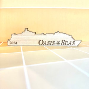 K&ouml;nnte beinhalten: Ein Holzausschnitt eines Kreuzfahrtschiffs mit dem Text "Oasis of the Seas" und "2024" darauf.