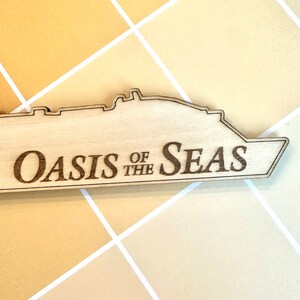 K&ouml;nnte beinhalten: Ein Holzausschnitt eines Kreuzfahrtschiffs mit dem eingravierten Text "Oasis of the Seas".