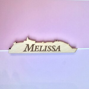 K&ouml;nnte beinhalten: Holzschnitt eines Kreuzfahrtschiffs mit dem eingravierten Namen "Melissa". Der Schnitt ist hellbraun und hat eine nat&uuml;rliche Holzmaserung.