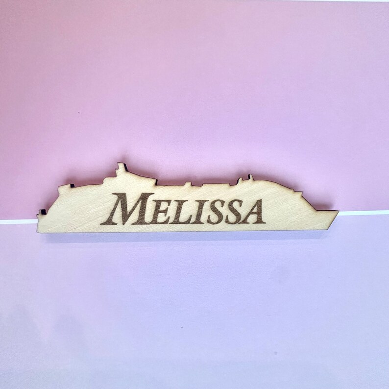 K&ouml;nnte beinhalten: Holzschnitt eines Kreuzfahrtschiffs mit dem eingravierten Namen "Melissa". Der Schnitt ist hellbraun und hat eine nat&uuml;rliche Holzmaserung.