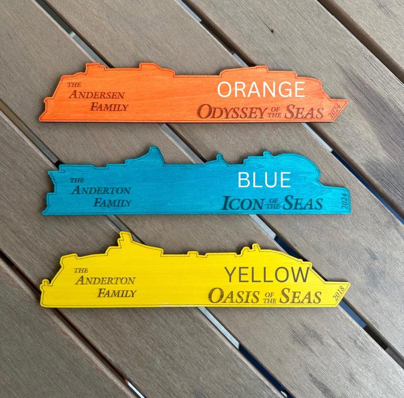 K&ouml;nnte beinhalten: Drei Holz-Schiffs-Umrisse, in Orange, Blau und Gelb bemalt. Jedes Schiff tr&auml;gt den Namen der Reederei und das Baujahr. Das orangefarbene Schiff ist die "Odyssey of the Seas", gebaut im Jahr 2021. Das blaue Schiff ist die "Icon of the Seas", gebaut im Jahr 2024. Das gelbe Schiff ist die "Oasis of the Seas", gebaut im Jahr 2018.