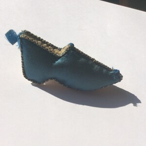 Puede incluir: Una zapatilla de fieltro azul con ribetes dorados. La zapatilla es un objeto decorativo pequeño.
