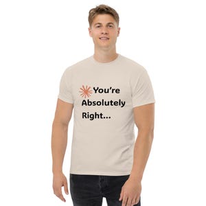 May include: A cream-coloured t-shirt featuring the phrase "You're Absolutely Right..." in black, with an orange burst graphic. The short-sleeved shirt is made of a soft material. The t-shirt is a casual wear item.