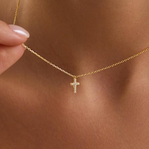 May include: A delicate gold necklace featuring a small cross pendant adorned with sparkling gemstones. The cross is centered on a fine gold chain. The necklace is displayed against a neutral background, highlighting the jewelry's elegance.