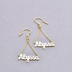 May include: Gold dangle earrings with the name "Alyssa" spelled out in cursive on each earring.