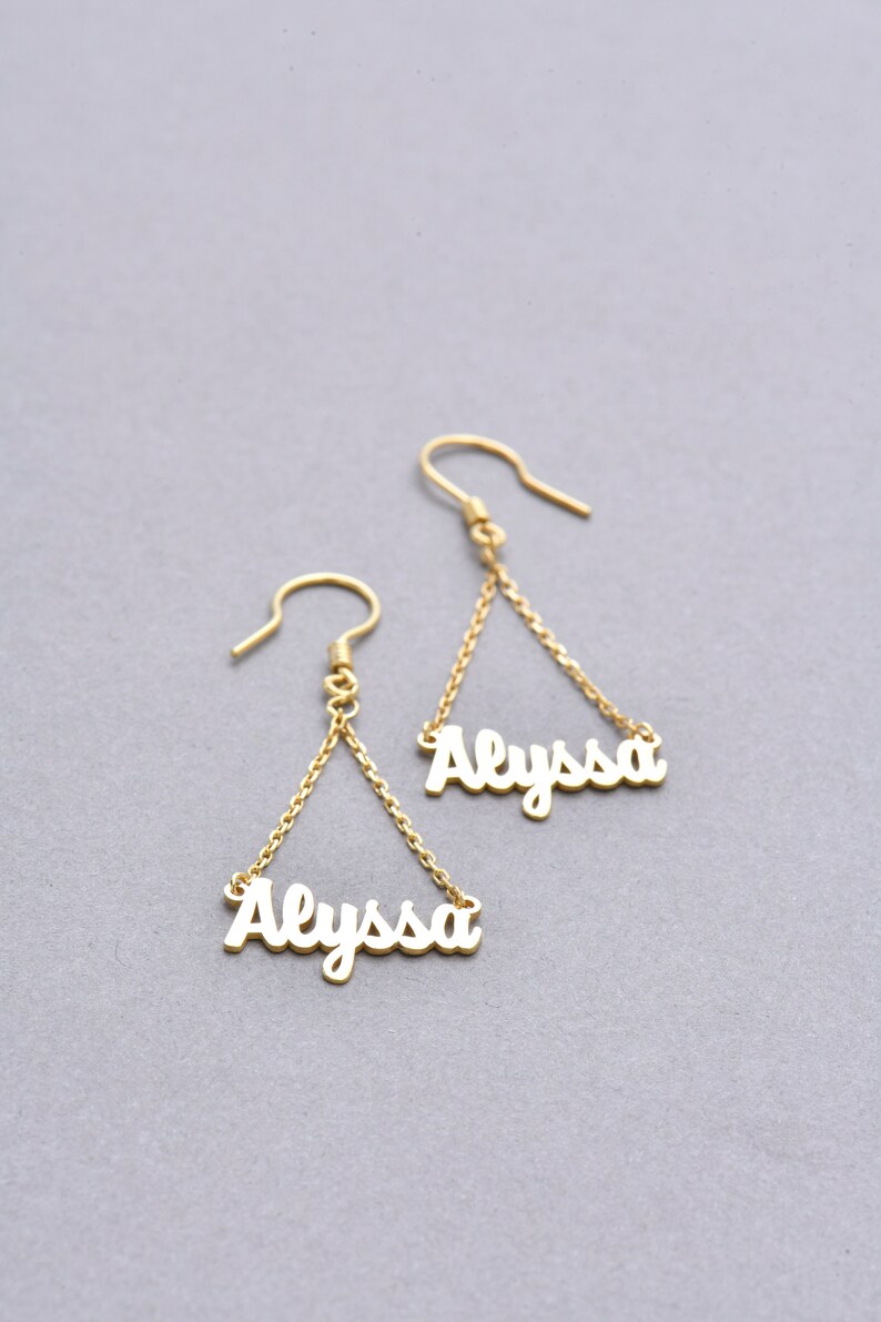 May include: Gold dangle earrings with the name "Alyssa" spelled out in cursive on each earring.