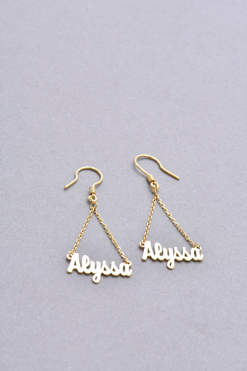 May include: Gold dangle earrings with the name "Alyssa" spelled out on each earring.
