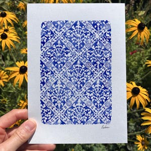 May include: A rectangular white paper print featuring a repeating blue watercolor pattern of intricate diamond shapes and floral motifs. The design resembles traditional tile work, and the word "lisbon" is written in small black script in the corner.
