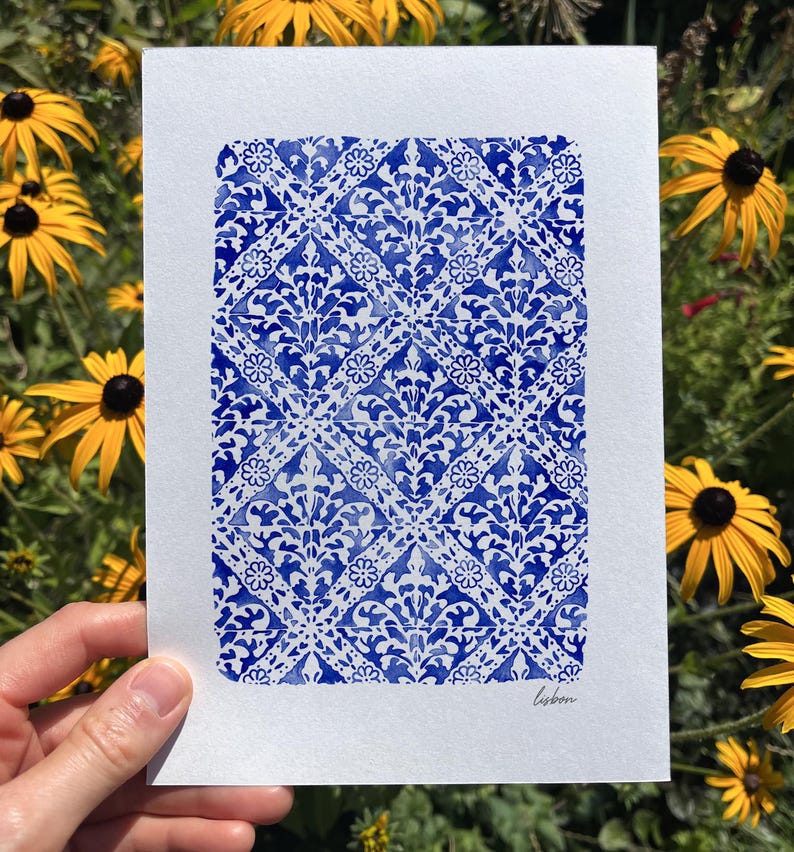 May include: A rectangular white paper print featuring a repeating blue watercolor pattern of intricate diamond shapes and floral motifs. The design resembles traditional tile work, and the word "lisbon" is written in small black script in the corner.