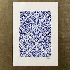 May include: A rectangular white paper print featuring a repeating blue watercolour pattern of diamonds and floral motifs. The design is arranged in a grid, and the word "lisbon" is handwritten in small black cursive letters in the bottom right corner.