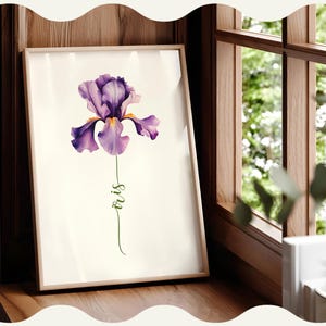 May include: A framed art print showing a watercolour illustration of a purple iris flower. The flower has detailed petals and a yellow centre. The word "iris" is written in green script below the flower. The artwork is displayed on a wooden surface near a window.