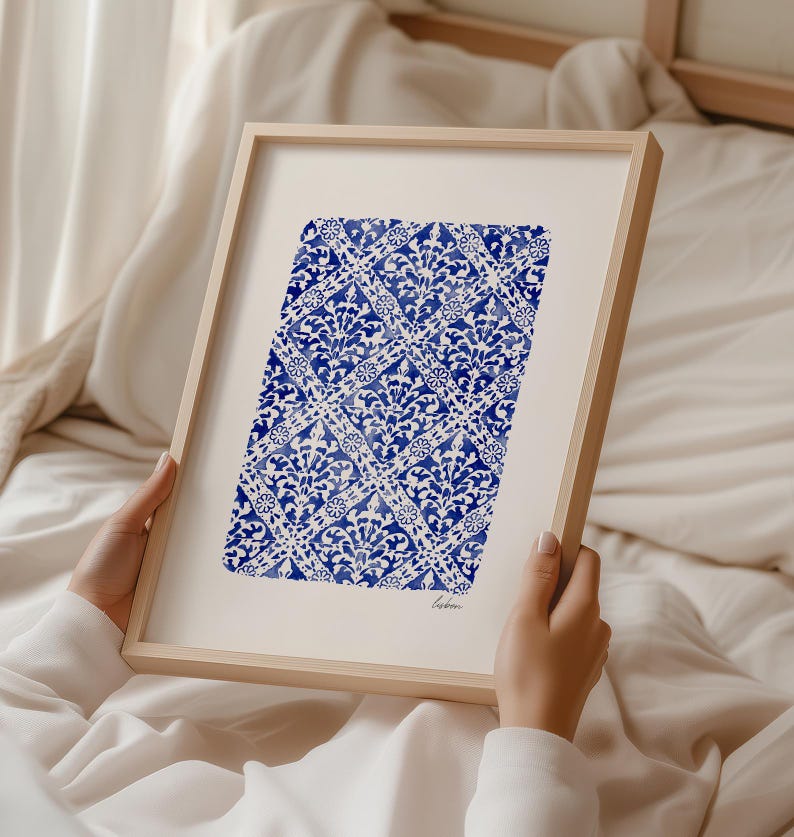 May include: A framed art print featuring a blue and white watercolor pattern of repeating diamond shapes filled with intricate floral motifs. The artwork is set against a white background within a light wood frame and includes the word Lisbon.