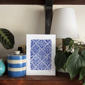 May include: A rectangular white art print featuring a repeating blue and white damask-style pattern arranged in a diamond grid. The print has a hand-painted watercolor texture and includes the word Lisbon written in small script at the bottom right.