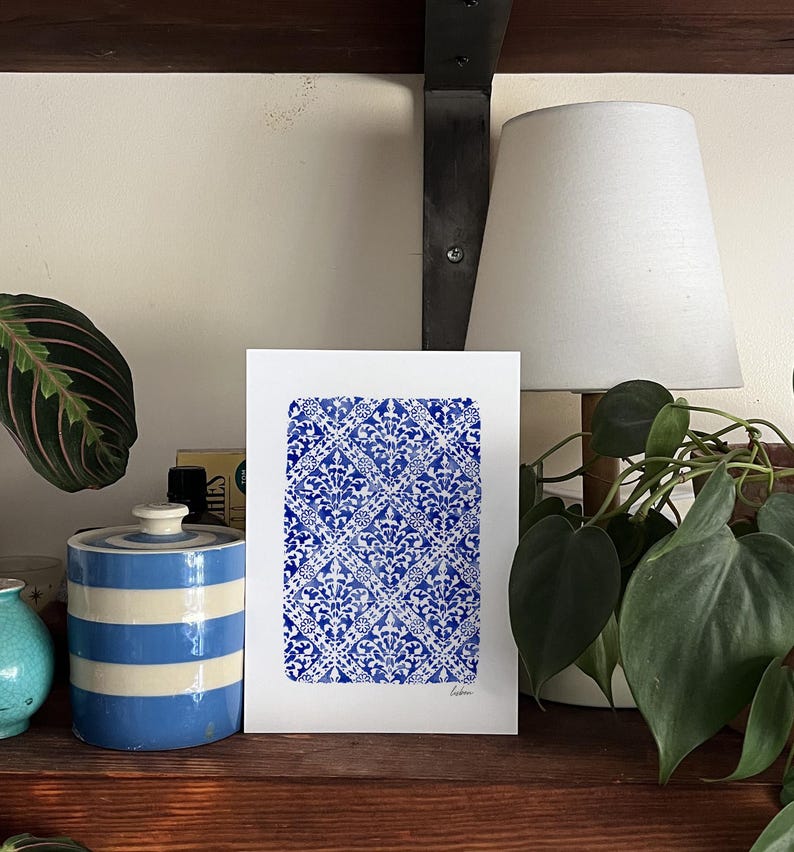 May include: A rectangular white art print featuring a repeating blue and white damask-style pattern arranged in a diamond grid. The print has a hand-painted watercolor texture and includes the word Lisbon written in small script at the bottom right.