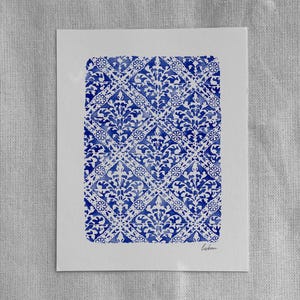 May include: A rectangular white paper print featuring a repeating blue watercolor pattern of diamonds, floral motifs, and intricate scrollwork. The word "lisbon" is written in small, cursive, dark gray script in the bottom right corner of the print.