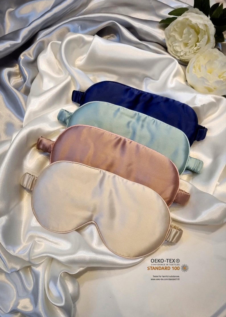 May include: Four silk sleep masks in different colors: navy blue, light blue, blush pink, and cream. The masks are stacked on top of each other on a white satin background. The masks are made of 100% silk and are certified by OEKO-TEX STANDARD 100, which means they are tested for harmful substances.