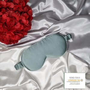 May include: A light blue satin sleep mask with an elastic band. The mask has the OEKO-TEX&reg; STANDARD 100 logo and text: "CONFIDENCE IN TEXTILES  STANDARD 100  13.JATR.90133 HOHENSTEIN HTTI  Tested for harmful substances  www.oeko-tex.com/standard100"