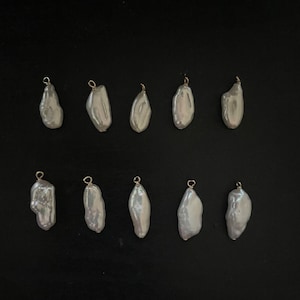 May include: Ten white baroque pearl pendants with gold jump rings. The pearls are irregular in shape and have a slightly off-white colour.