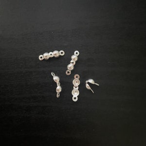 May include: Five silver metal bead caps for jewellery making. The caps are in different shapes and sizes, with some having a loop on one end.