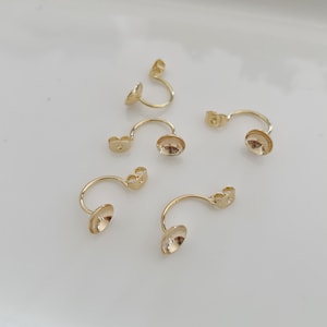 Könnte beinhalten: Fünf goldfarbene Ohrring-Findings mit einem gebogenen Draht und einer runden Tasse am Ende.